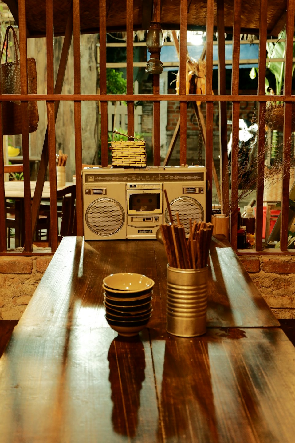 A vintage silver boombox sits on a shelf behind wooden slats.