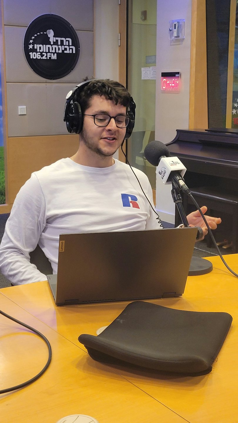 Man with glasses and headphones speaks into a studio microphone.